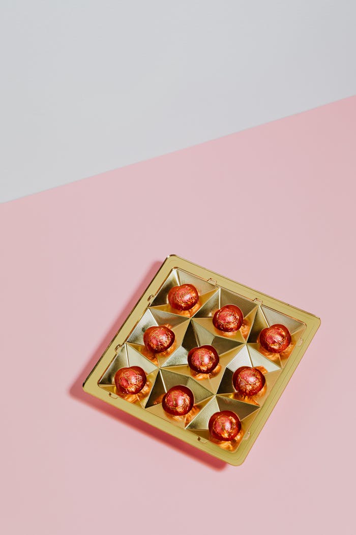 Delicious wrapped chocolate pralines displayed elegantly on a pink surface with golden casing.
